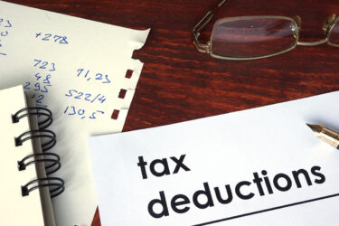 Tax Deductions typed out on a piece of paper with another piece of paper nearby that has handwritten numbers on it.