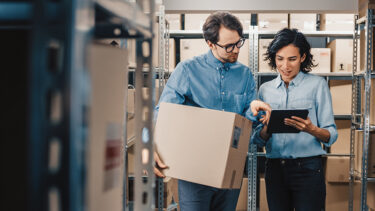 Inventory Manager Shows Digital Tablet Information to a Worker Holding Cardboard Box.