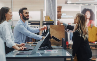 New retail employee shadowing another retail clerk and helping a woman with a purchase.