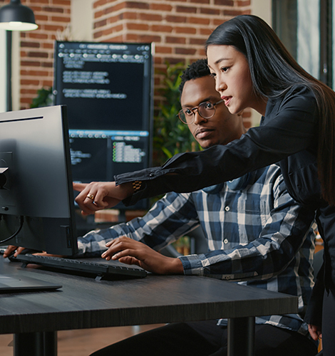 Two security compliance techs looking at code on a desktop computer.