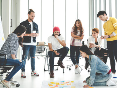 Group of seven young people meeting and looking at project plan lay out on floor discuss or brainstorm business strategy with post note.