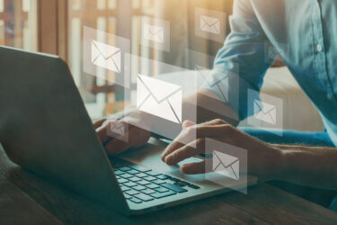 Woman sitting at a computer with email icons floating around the computer.