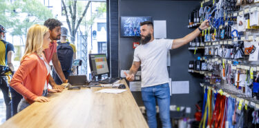 A Female and Male customer in a retail store looking at product with a cashier. NCR Counterpoint point of sale software is displayed on the register in the background.