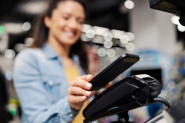 Woman using a phone to checkout in a retail store. Payment terminal uses encryption to prevent cybersecurity attacks.